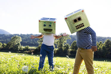 Boys covered face with smiling and robot box while playing in meadow - VABF03515
