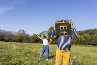 Brothers enjoying playing with robot and smiling cardboard box in meadow - VABF03524