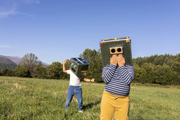 Jungen spielen mit Roboterkarton, während sie auf einer Wiese stehen - VABF03525