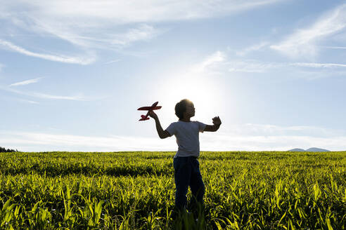 Silhouette eines Jungen, der mit einem Flugzeugspielzeug gegen den klaren Himmel spielt - VABF03536
