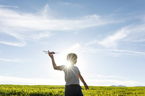 Playful boy holding airplane toy while standing against clear sky stock photo