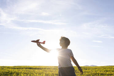 Junge, der mit einem Flugzeug spielt, während er vor einem klaren Himmel steht - VABF03542