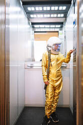Boy wearing space suit pressing buttons in open elevator - JCMF01472