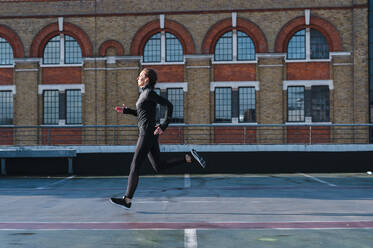 Mid adult woman running on rooftop against building in city - JMPF00410