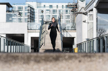 Female athlete running on rooftop in city during sunny day - JMPF00414