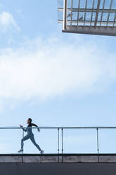 Weibliche Athletin läuft auf dem Dach gegen den Himmel an einem sonnigen Tag - JMPF00419