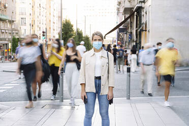 Junge Frau mit Maske steht auf der Straße in der Stadt - JCMF01488