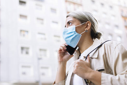 Close-up of young woman wearing mask talking over smart phone in city - JCMF01490