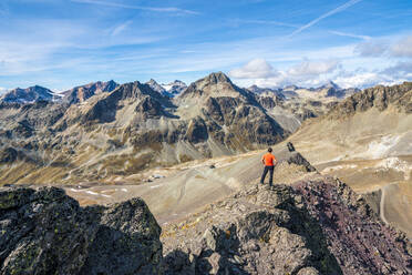 Rear view of man on top of Piz Nair looking towards Piz Suvretta mountain peak, Engadine, canton of Graubunden, Switzerland, Europe - RHPLF17548