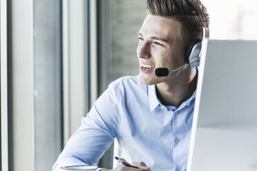 Close-up of smiling male customer representative talking over headset in call center - UUF21480