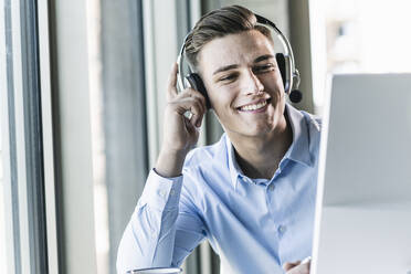 Close-up of smiling male customer representative talking over headset in office - UUF21481