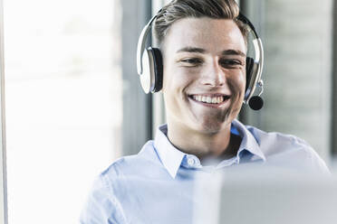 Close-up of smiling salesman talking over headset in office - UUF21482