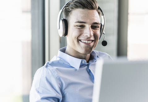 Nahaufnahme eines lächelnden Geschäftsmannes, der über ein Headset in einem Callcenter spricht - UUF21483