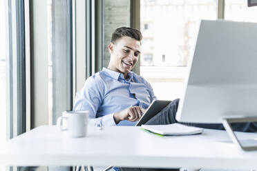 Lächelnder Geschäftsmann mit digitalem Tablet am Schreibtisch im Büro - UUF21484