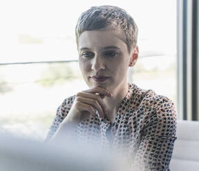 Close-up of thoughtful businesswoman with short hair sitting in office - UUF21490