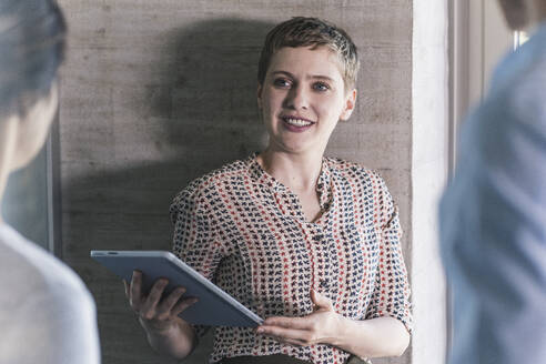 Businesswoman holding digital tablet discussing with male and female colleagues in office - UUF21506