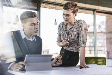 Male and female professionals discussing at desk in office - UUF21507