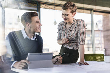 Lächelnde Geschäftspartner, die am Schreibtisch im Büro diskutieren - UUF21508