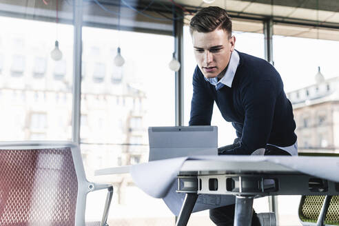 Männlicher Berufstätiger, der über einem digitalen Tablet arbeitet, während er auf einem Schreibtisch im Büro sitzt - UUF21519