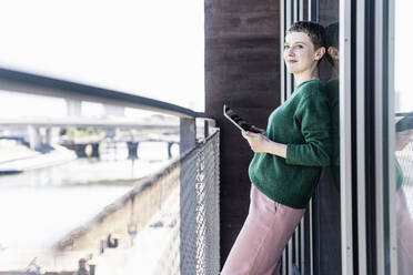Nachdenkliche Geschäftsfrau mit digitalem Tablet auf dem Balkon im Büro - UUF21539
