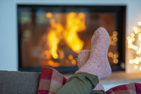 Legs of young woman wearing socks relaxing against fireplace at home - LBF03232