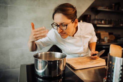 Weibliche Köchin riecht heißes Essen beim Kochen in der Restaurantküche - CAVF89272