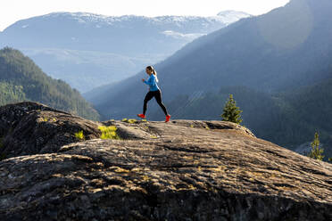 Side view of strong sportswoman running against snowy mountain ridge during fitness workout in countryside at sunset. - CAVF89290