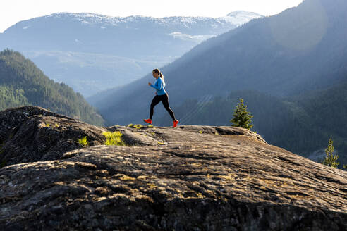 Seitenansicht einer starken Sportlerin, die während eines Fitnesstrainings auf dem Lande bei Sonnenuntergang gegen einen verschneiten Bergrücken läuft. - CAVF89290