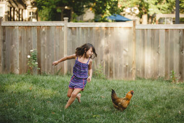 Ein glückliches Kind spielt barfuß mit einem Huhn in seinem Garten - CAVF89313