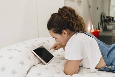 Mädchen, das ein digitales Tablet benutzt, während es zu Hause auf dem Bett liegt - DGOF01446