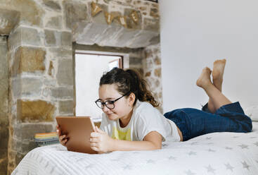 Girl lying on front while using digital tablet at home in bedroom - DGOF01448