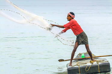 Ein Fischer wirft ein beschwertes Netz auf einem kleinen Floß vor dem beliebten Marari Beach, Mararikulam, Alappuzha (Alleppey), Kerala, Indien, Asien - RHPLF17623