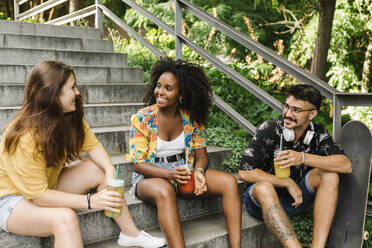 Freunde sitzen auf den Stufen und trinken Saft in einem öffentlichen Park - XLGF00565