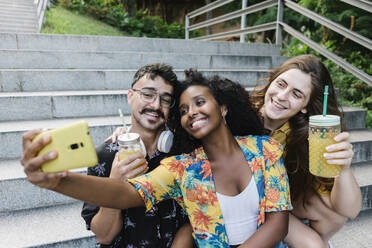 Friends taking selfie on smart phone while sitting in public park - XLGF00570