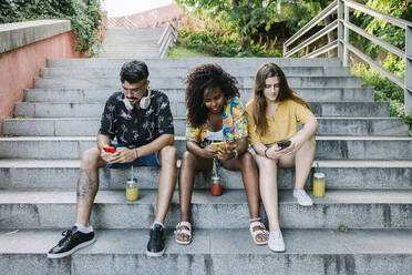 Young friends text messaging on smart phone while sitting on steps in park - XLGF00571