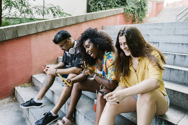 Young woman taking selfie while friends text messaging on smart phone sitting on steps - XLGF00572