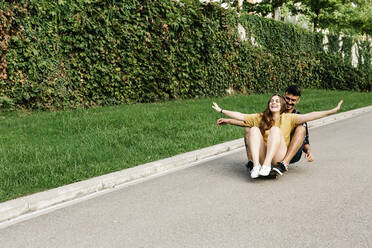 Freunde genießen das Fahren auf dem Skateboard mit ausgestreckten Armen im Park - XLGF00577