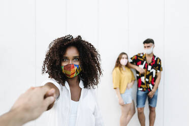 Man holding young woman hand while friends standing against white wall - XLGF00593