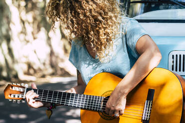 Mature woman with curly hair playing guitar while leaning on motor home - SIPF02194