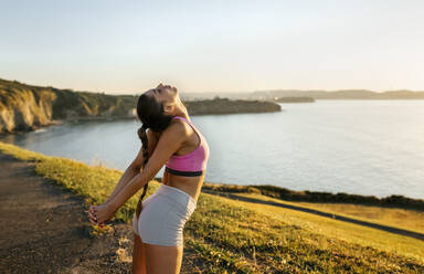 Young woman stretching hands while standing on cliff against clear sky during sunset - MGOF04467