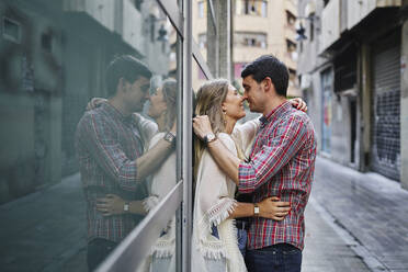 Reflecting image of couple nuzzling nose while standing on street in city - SASF00110