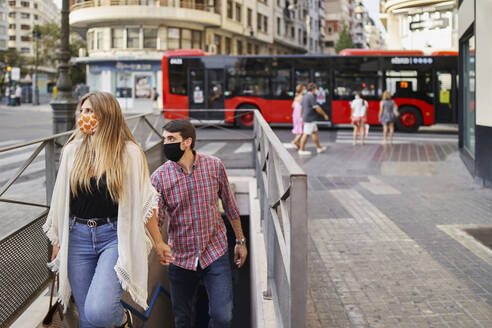 Couple wearing face mask climbing steps of subway in city - SASF00112