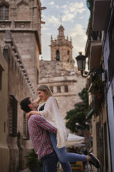 Happy man picking up woman while standing in city - SASF00122