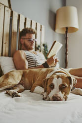 A young blond boy reading in bed with his dog - CAVF89417