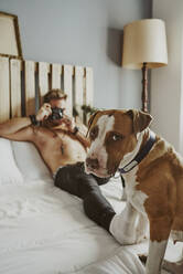 Ein junger blonder Junge, der seinen Hund im Bett fotografiert - CAVF89423