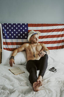 Ein junger Mann im Bett mit einem Hut und ohne Hemd mit dem amerikanischen Fla - CAVF89432