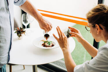 Frau fotografiert Essen mit Smartphone, während der Kellner das Essen serviert - CAVF89451