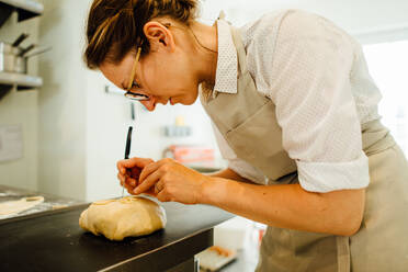 Bäckerin in Uniform dekoriert Brot bei der Arbeit in der Bäckerei - CAVF89455