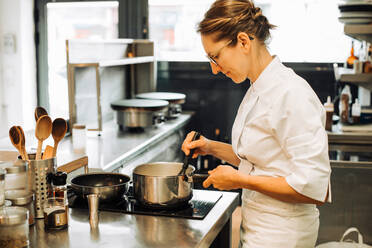 Weibliche Köchin bei der Arbeit in der Restaurantküche, rührt heißes Essen in der Pfanne um - CAVF89476