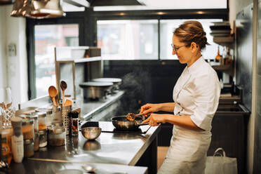 Female chef stirring hot food while working in restaurant kitchen - CAVF89480